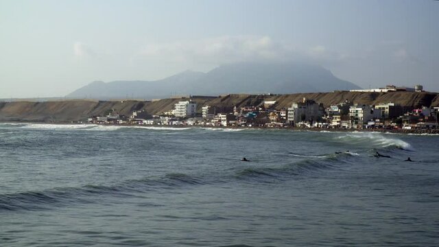 Surfers Riding the Waves with a Scenic Landscape View of the Ocean and Mountainous Background in Huanchaco, Trujillo, La Libertad, Peru