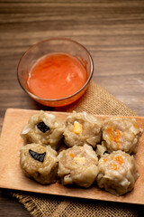 Dimsum and a bowl of orange sambal on wooden table and wooden plate