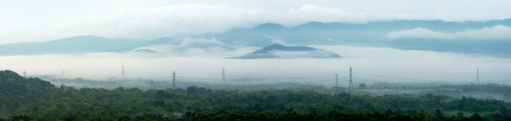 Panorama aerial view transmission tower in green forest and beautiful morning smooth fog. Energy and environment concept. High voltage power poles. mae moh, lampang.
