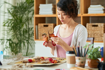 Inspired creative young woman cutting dried orange leaf when practicing oshibana at home