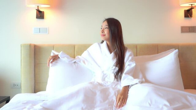Happy woman lying on the bed in white bathrobe dreaming looking at the window daytime