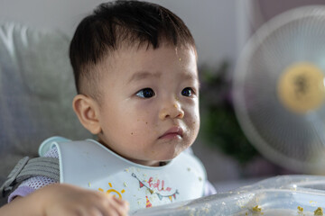 adorable and cute happy Asian Chinese baby boy siting on baby chair enjoying his lunch