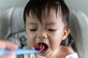 adorable and cute happy Asian Chinese baby boy siting on baby chair enjoying his lunch