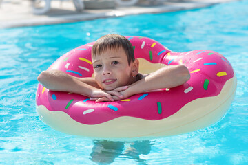 Happy little boy with variegated life ring in the form of a donut has fun in the swimming pool