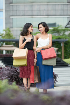 Happy pretty young women walking outdoors after buying a lot of shoes, clothes and cosmetics on sale in mall