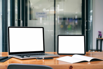 Mockup blank white screen laptop and tablet on wooden table in modern office room.