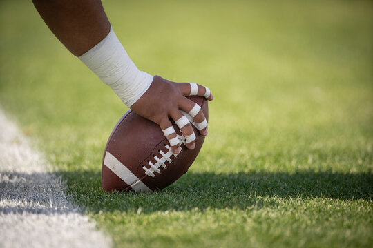 Hiking the football in a football game. Focus on the hands and the details of the football. 