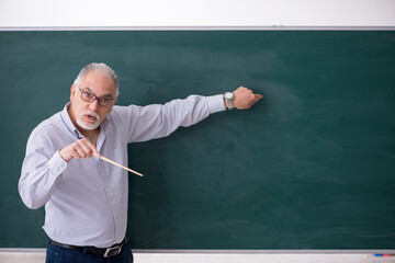 Old male teacher in front of green board