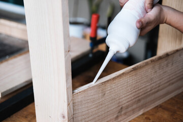 Woodworking operators are using glue to put together the wood parts to assemble and build a wooden table for their customers.