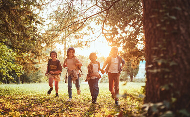 Excited children with backpacks enjoying walk in forest on sunny autumn day, kids exploring nature