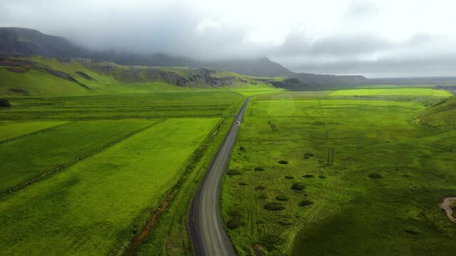 Aerial shot of car driving down road in the green countryside of Iceland and water droplets hitting the camera lens