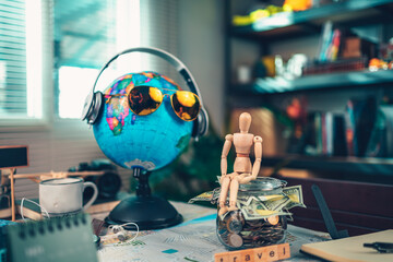 Wood human doll sitting on Saving money in glass jar for travel, holiday, vocation on road map on the table. Travel budget concept.