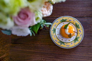 Obraz na płótnie Canvas 木のテーブルにのったピンクのバラやトルコ桔梗の小さなブーケとオレンジの一人前のプチケーキ