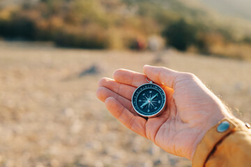 Point of view. The compass lies in a man's palm against the backdrop of a mountain landscape. - 453738284