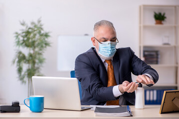 Old male employee working in the office during pandemic