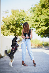 Young stylish woman standing and playing with her siberian husky in city