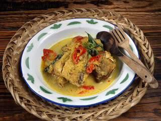 Mangut ikan pe or pari or spicy fish curry is Javanese cuisine. Smoked stingray fish cooked with spices and coconut milk. Focus selection, rustic wooden background. 