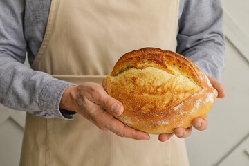 Male baker with fresh bread on grey background, closeup