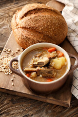 Pot with tasty beef barley soup and loaf of bread on wooden background