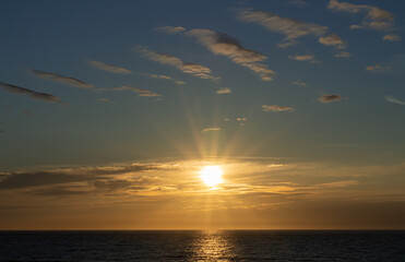 Zachodzące słońce, chowające się za horyzontem morza na tle przepięknych chmur i kolorystycznego niebieskiego nieba