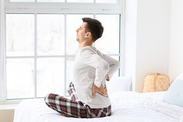 Young man suffering from back pain in bedroom