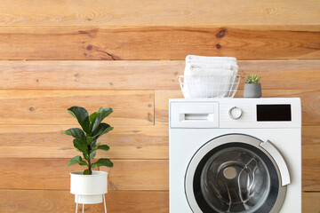 Modern washing machine with towels near wooden wall