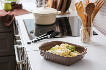 Baking dish with raw stuffed cabbage rolls on table in kitchen