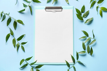 Clipboard with blank sheet of paper and green leaves on color background