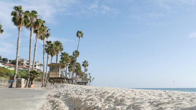 Tropical palm trees, white sandy beach by sea water wave, pacific ocean coast, San Clemente California USA. Blue sky and lifeguard tower. Life guard watchtower hut, summertime shore. Los Angeles vibes