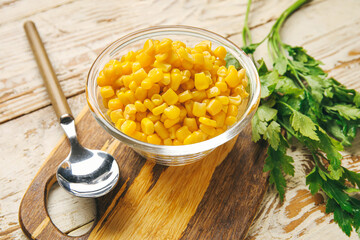Bowl with corn kernels and parsley on light wooden background, closeup