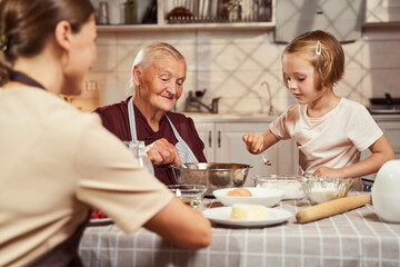 Obraz na płótnie Canvas Pensioner mixing up dough with girl adding flour