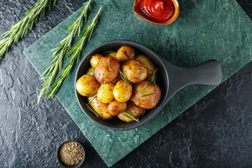 Frying pan with baked potatoes and rosemary on dark background