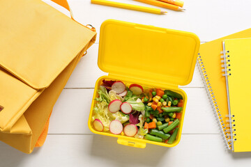 Lunch box with vegetables, bag and stationery on light wooden background
