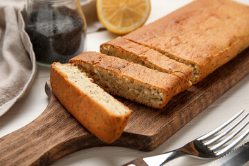 Wooden board with delicious poppy seed cake on table