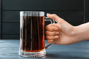 Female hand with mug of fresh kvass on dark wooden background - obrazy, fototapety, plakaty