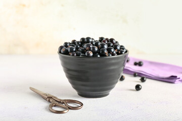 Fototapeta na wymiar Bowl with ripe black currant and scissors on light background