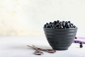 Fototapeta na wymiar Bowl with ripe black currant and scissors on light background