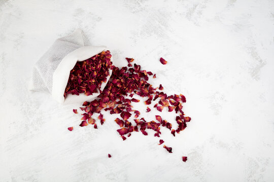 Dried rose petals in pouch, top view. Light background, copy space. Pink colored organic herb used for perfumes, cosmetics, teas and baths. Red dry petals