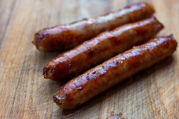 
Three freshly fried sausages lie diagonally on a wooden board. Fat protruding is visible