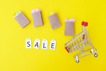 Shopping cart with paper bags and white labels with the word SALE on a yellow background.