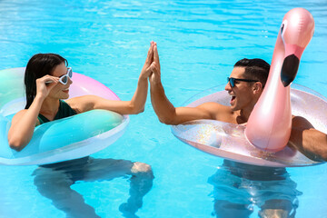 Young couple with inflatable rings giving each other high-five in swimming pool