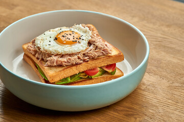 French sandwich Croque Madame with egg, cucumber, tomatoes, avocado and tuna in a plate on a wooden background