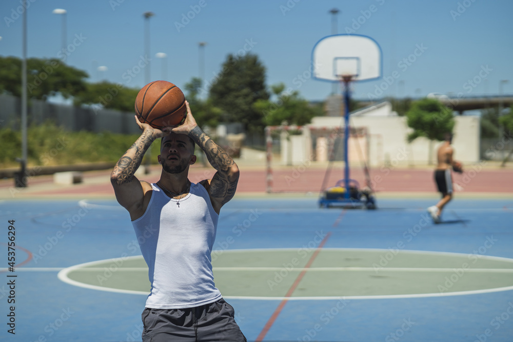 Wall mural handsome caucasian basketball player with cool tattoos standing on the court throwing the ball up