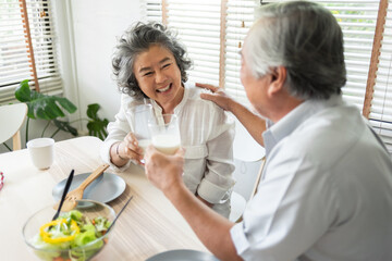 Smiling Asian senior couple drinking glasses of milk at home