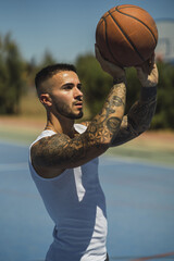 Handsome caucasian basketball player with cool tattoos standing on the court throwing the ball up