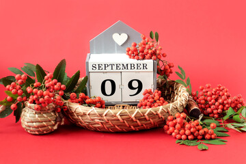 Calendar for September 9 : the name of the month in English, cubes with the numbers 0 and 9 on a decorative tray, branches of red mountain ash around on a crimson background, side view