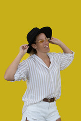 Portrait of beautiful woman holding black cowboy hat on yellow background