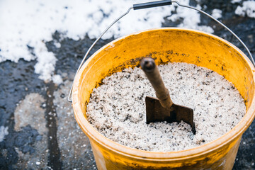 Road or thawing salt into a yellow bucket, icy ground
