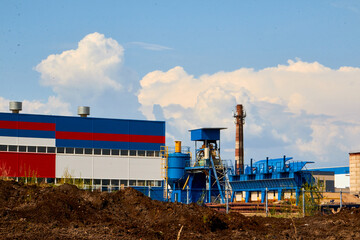 Fototapeta na wymiar Building of plant or factory in rural place framed by tree branches and shrubs and blue sky with white clouds