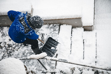 Man is clearing the snow on staircases, snow pusher and shovelling - obrazy, fototapety, plakaty